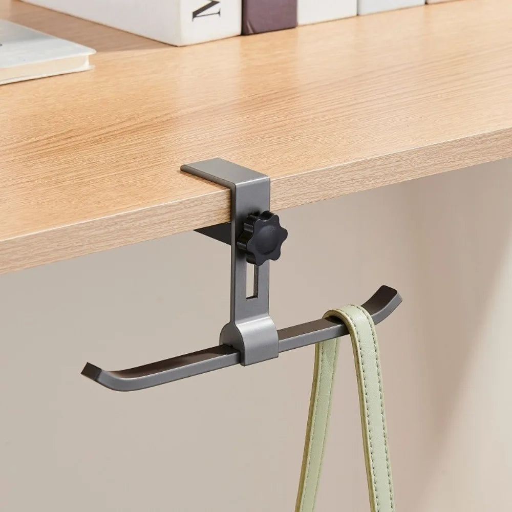 A silver adjustable aluminum desk hook with dual clips is shown hanging from a wooden shelf.