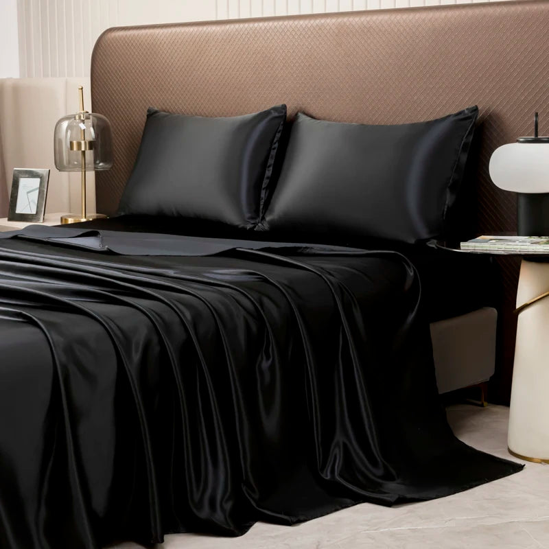 Black satin flat bed sheet set with two pillows draped over a beige headboard.