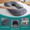 Gray ergonomic J-shaped maternity pillow with a zipper closure and plush material shown on a white bed.