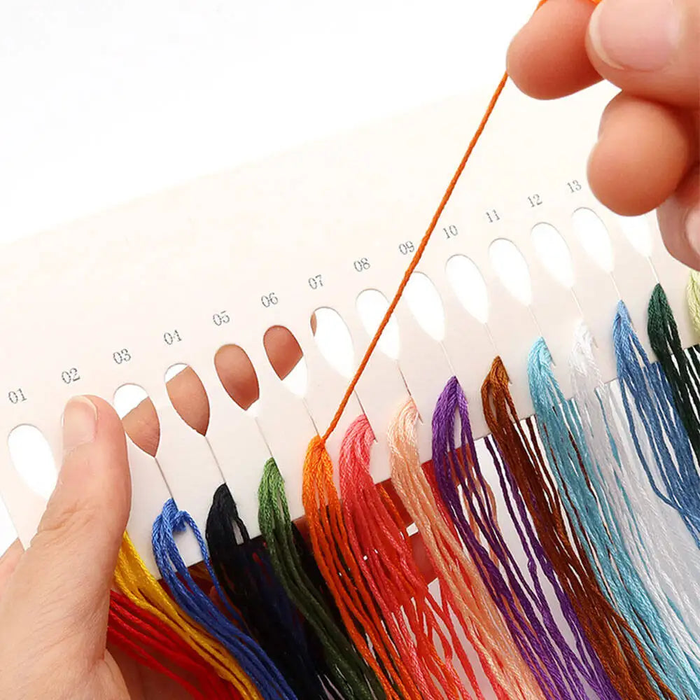 A hand holds a set of mini flower cross stitch vase threads in various colors like red, yellow, blue, and purple.