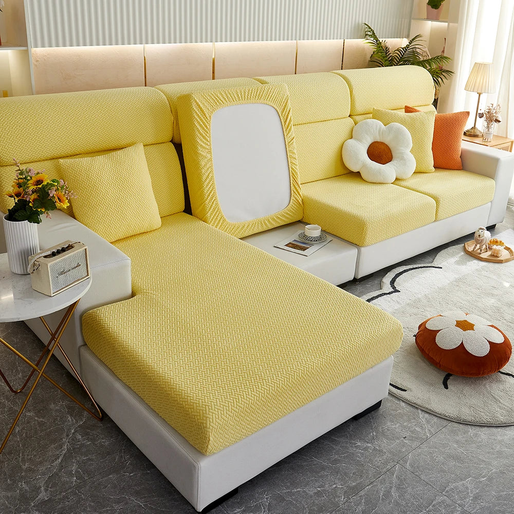 A yellow Jacquard elastic sofa slipcover with white accents and orange pillows in a bright living room setting.