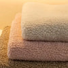 Three fluffy sherpa anti-slip sofa covers stacked on a surface in shades of white, pink, and beige.