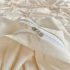 A close-up of a light beige pinch pleat duvet cover set for king size bedding showing a white zipper detail.