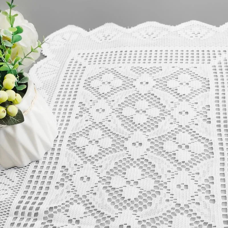 White lace table runner with a decorative pattern and a small white flower arrangement.