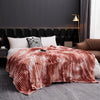 A fluffy tie-dye flannel fleece throw blanket in shades of pink and white draped over a bed.