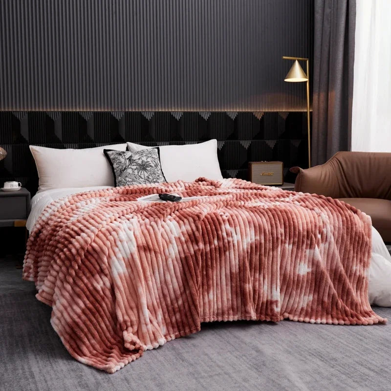 A fluffy tie-dye flannel fleece throw blanket in shades of pink and white draped over a bed.