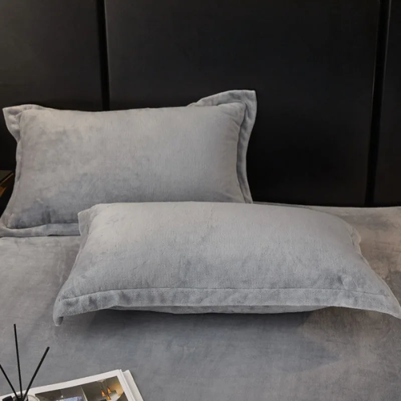 Two light gray velvet pillows resting on a dark surface against a black background.