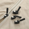 A black zipper repair kit with five detachable pulls is shown against a beige fabric background.