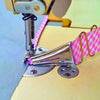 A close-up of a pink patterned bias binder being fastened to a piece of fabric using a sewing machine.