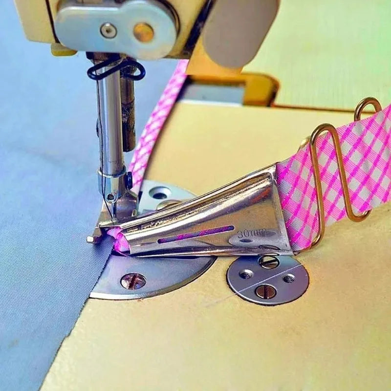 A close-up of a pink patterned bias binder being fastened to a piece of fabric using a sewing machine.