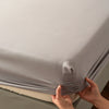 Hands adjusting a gray soft touch microfiber fitted sheet with deep pockets on a bed.