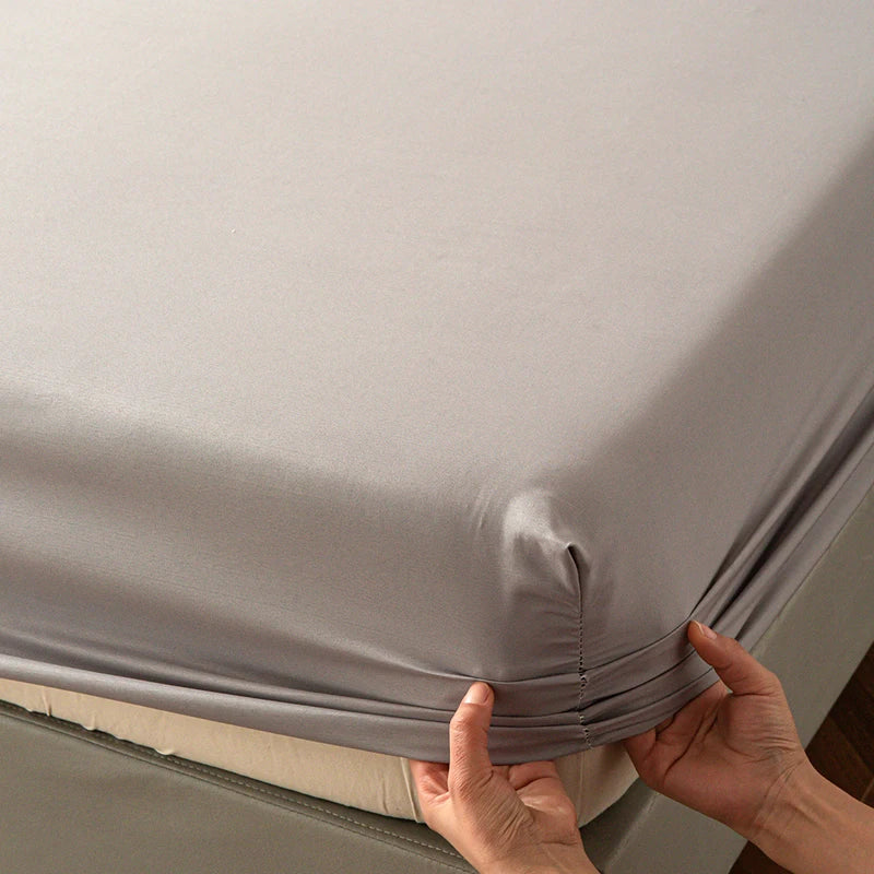 Hands adjusting a gray soft touch microfiber fitted sheet with deep pockets on a bed.