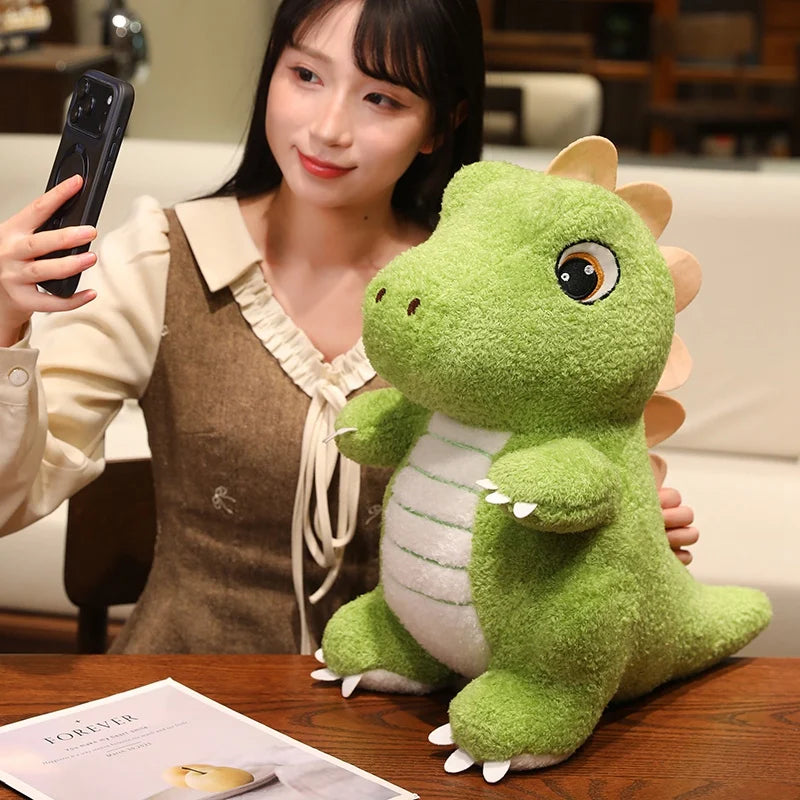 A cute green dinosaur plush toy is displayed on a wooden table next to a person.