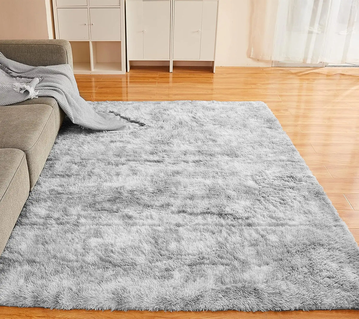 A fluffy gray tie-dyed plush floor mat placed on a wooden floor in a bright room.