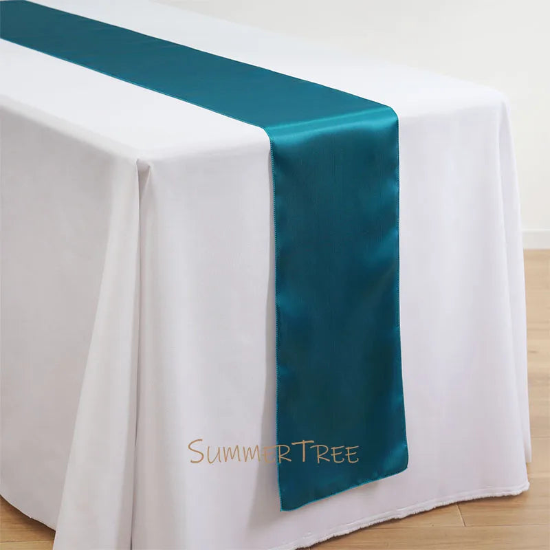 Elegant satin teal table runner draped across a white tablecloth.