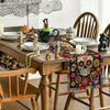 A wooden dining table set for a meal featuring a colorful skull and floral day of the dead table runner.