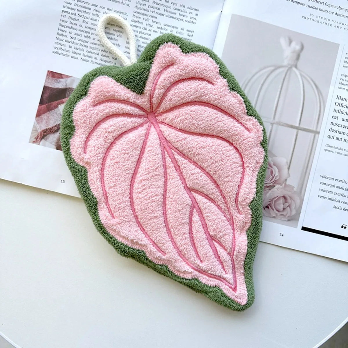 A heart-shaped hand towel made of green and pink textured fabric is displayed on a white surface.