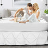 A couple relaxing on a white bed with a white duvet and a white bed skirt.