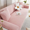 A pink stretchable sofa cover with white decorative pillows and a glass of water on the seat.