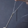 A hand is using a stainless steel hand sewing needle to thread white thread.