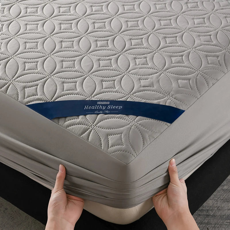 A gray quilted mattress protector labeled Healthy Sleep is being held by hands.
