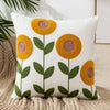 White throw pillow cover with embroidered yellow and brown floral designs on a beige knitted surface.
