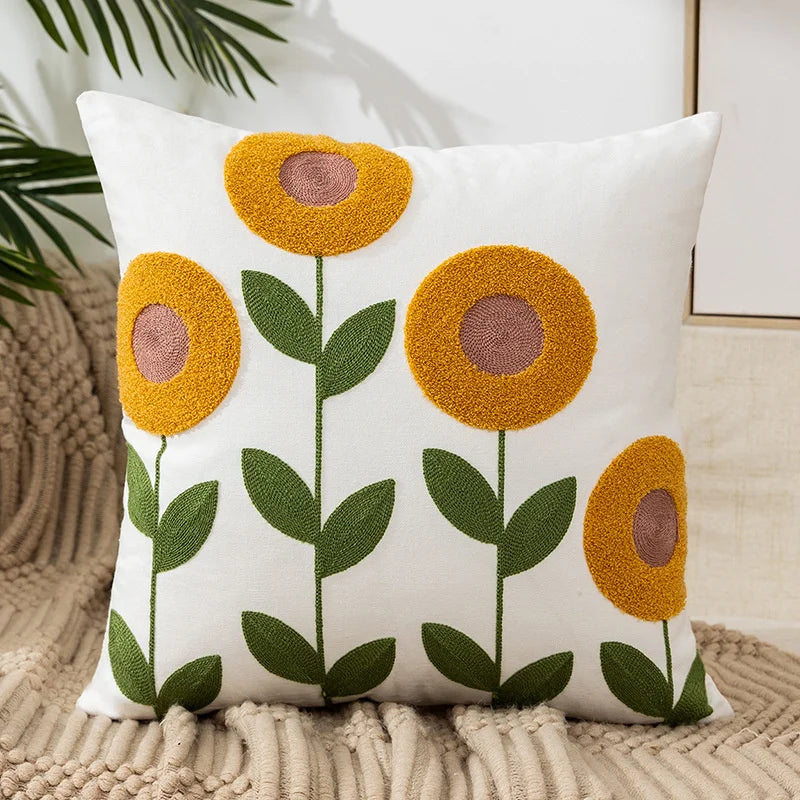 White throw pillow cover with embroidered yellow and brown floral designs on a beige knitted surface.