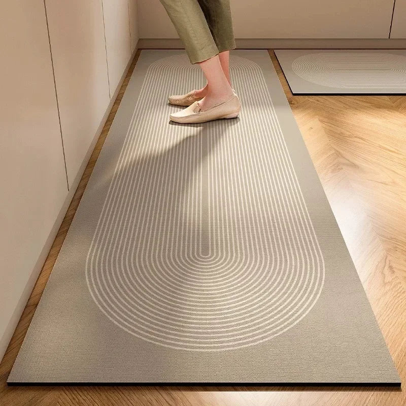 A person's feet are standing on a light gray kitchen floor mat with concentric circular patterns on a wooden floor.