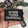 A black iron-on patch with white text that reads My mom thinks I'm special, held in a hand among other patches.