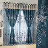 A pair of teal embroidered dual-layer curtains with sheer overlays hanging in a window.