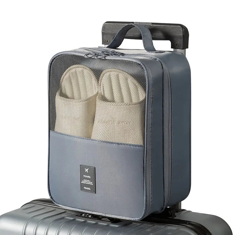 A gray portable travel shoe organizer bag with a handle is placed on a silver suitcase.