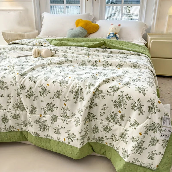 A white quilt with a green border and floral print is displayed on a bed with yellow and blue stuffed animals.