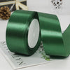 A roll of dark green satin ribbon with a white center, lying on a piece of paper.