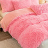 A pink plush duvet cover set with a matching pink fluffy blanket and pillows on a bed.