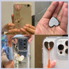 A hand holds a phone case with a metal heart charm connector attached, showcasing the decorative accessory.