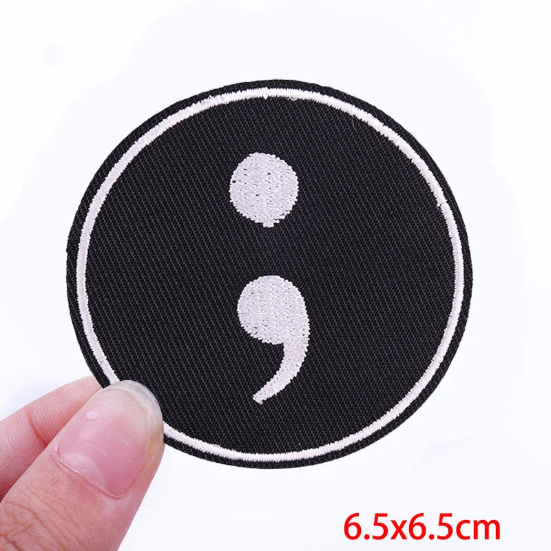 Black embroidered patch with white speech bubble symbol on a finger