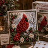 A framed piece of vintage Christmas fabric art featuring a red bird surrounded by green foliage and white snow.