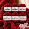 A set of six red wool yarn skeins labeled Fancy Wool stacked on a red knitted fabric.