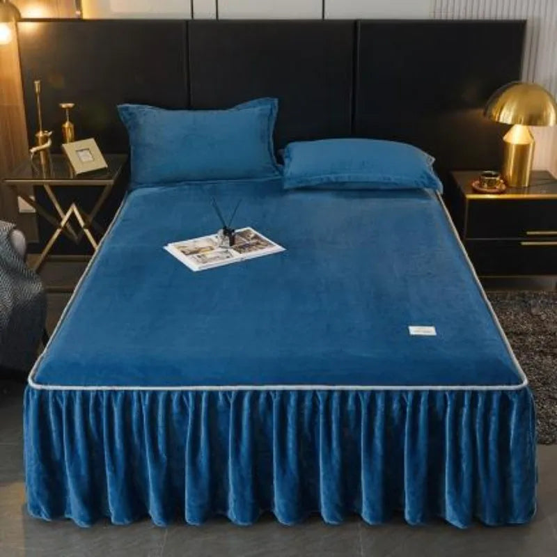 A deep blue velvet bed skirt with a ruffled hem is displayed over a bed, set against a dark background.