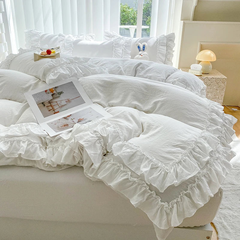 A white 3-piece ruffled duvet cover set displayed on a bed with sheer white curtains and natural light.