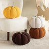 Three textured fabric pumpkins in yellow, white, and brown are displayed on a light-colored surface.