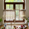 Beige gingham crochet lace curtain valance hanging in a wooden window frame.