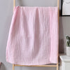 A pink, textured cotton gauze blanket hanging on a wooden hanger against a gray wall.