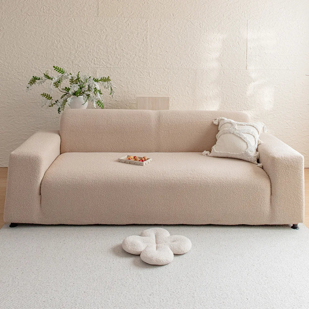 A light beige jacquard velvet sofa cover on a cream rug with a small plant and decorative pillows.