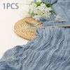 A light blue semi-sheer gauze fabric draped with ruffles, accompanied by a gold woven mat and silver cutlery.
