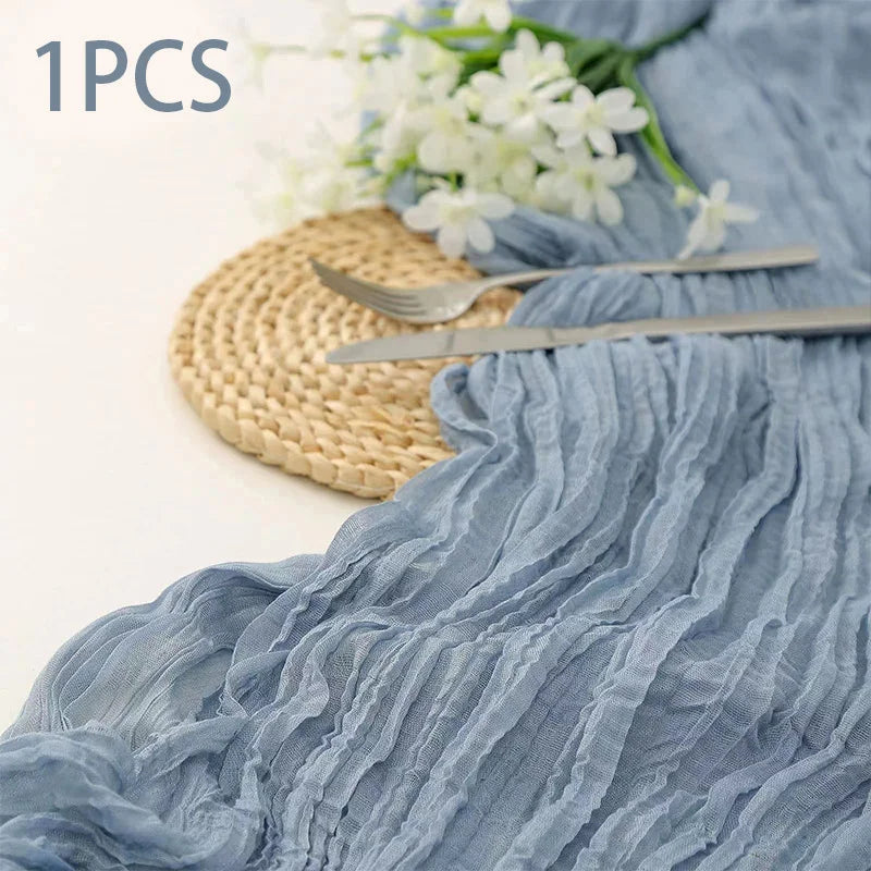 A light blue semi-sheer gauze fabric draped with ruffles, accompanied by a gold woven mat and silver cutlery.