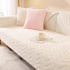 A pink throw pillow rests on a white quilted sofa seat cushion cover with a white blanket and a mug.