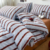 A bed covered with a striped duvet and pillow set featuring white and brown stripes.