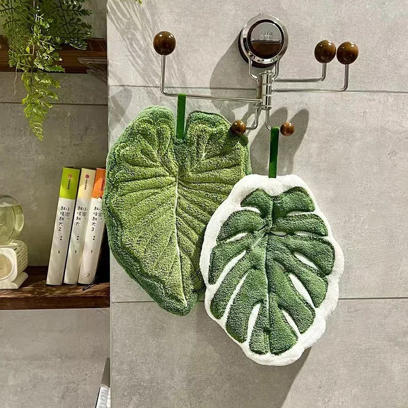 A hand towel with an embroidered leaf design hangs on a metal rack against a gray wall.
