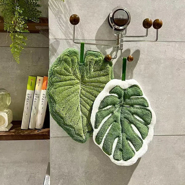 A hand towel with an embroidered leaf design hangs on a metal rack against a gray wall.